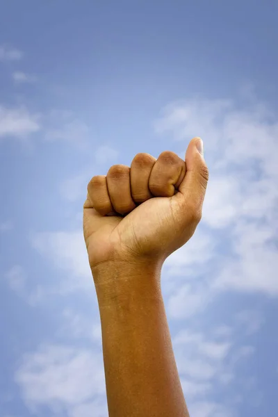 A fist clenched upwards with blue sky with some clouds in the background. Concept of anti-racist fight. Black movement.