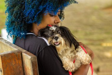 Saçları maviye boyanmış, kucağında köpek yavrusuyla parktaki bankta oturan siyahi bir kadın..
