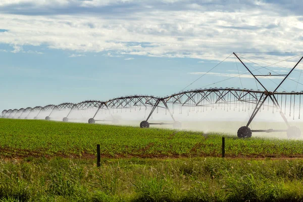 stock image Irrigation machine watering the growing crop, on a clear day with some clouds in the sky.