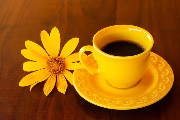 Gövde üzerinde sarı bir fincan kahve ve karanlık bir tahta masanın üstünde bir ayçiçeği..