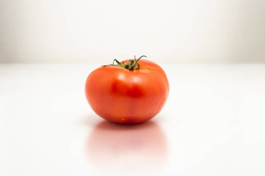 Beyaz arka planı olan beyaz bir yüzeyde büyük, taze, olgun bir domates..