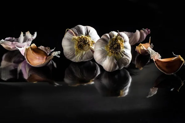 A few heads of garlic on a shiny black surface.