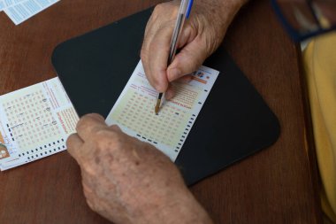 Piyango kartındaki rakamları işaretleyen yaşlı bir adamın ellerine yakın çekim..