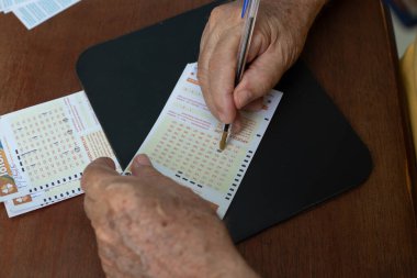 Piyango kartındaki rakamları işaretleyen yaşlı bir adamın ellerine yakın çekim..