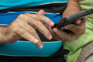 Cep telefonu kullanan yaşlı bir adamın ellerinin ayrıntıları..