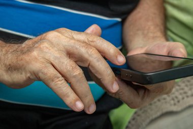 Cep telefonu kullanan yaşlı bir adamın ellerinin ayrıntıları..