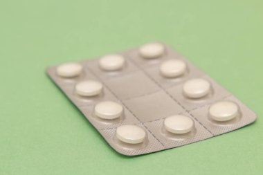 Yeşil bir yüzey üzerinde tabletleri olan plastik ve alüminyum kabarcık..