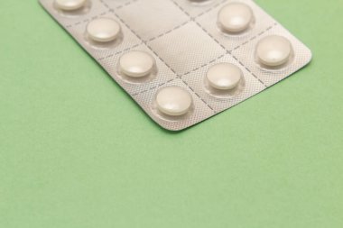 Detalhe de um blister com comprimidos sobre uma superficie de cor verde.