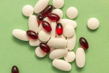 Yeşil bir yüzey üzerinde beyaz haplar ve kırmızı jelatinli kapsüller..