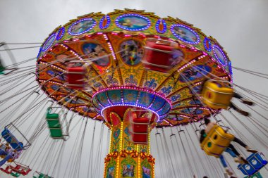 Renkli, dev bir döner oyuncak, hızla dönüyor, zincirlerle bağlanmış sandalyelerle, birkaç kişiyle, bir lunaparkta. Fotoğraf aşağıdan yukarıya düşük kamera hızında çekildi.
