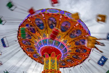 Bulutlu bir günde, eğlence parkında, zincirlerle bağlı sandalyelerle dönen dev bir dönme dolap. Fotoğraf aşağıdan yukarıya düşük kamera hızında çekildi.