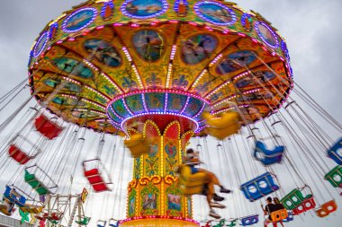 Bulutlu bir günde, düşük hızda koşan birkaç kişiyle lunaparkta dönen dev bir sürüşün ayrıntıları. Fotoğraf aşağıdan yukarıya doğru çekilmiş..