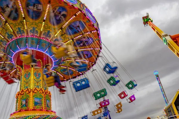 Detail of a giant spinning ride, spinning, in the amusement park with few people, on a cloudy day. Photo taken from bottom to top