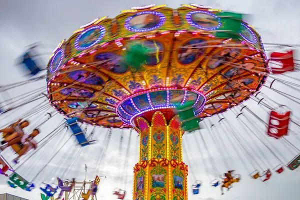 Bulutlu bir günde, eğlence parkında, zincirlerle bağlı sandalyelerle dönen dev bir dönme dolap. Fotoğraf aşağıdan yukarıya düşük kamera hızında çekildi.
