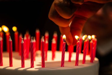 Doğum günü pastasına mum ve birkaç mum koyan bir elin ayrıntıları.