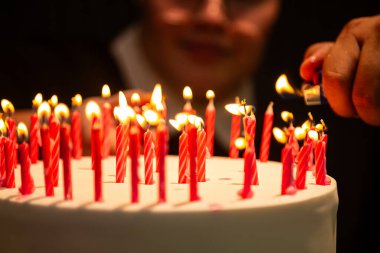  Arka planda bulanık bir yüz olan doğum günü pastasında mum yakan bir elin ayrıntıları.