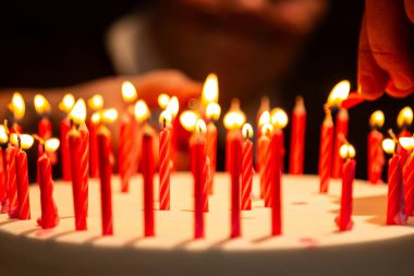 Arka planda bulanık bir yüz olan doğum günü pastasında mum yakan bir elin ayrıntıları.