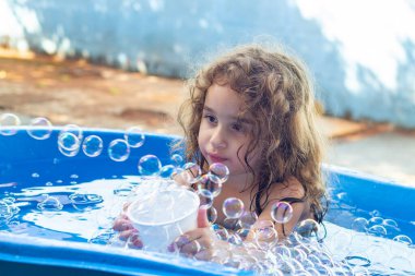 Mavi çocuk havuzunda bir çocuk, arka bahçede sabun köpüğüyle oynuyor..