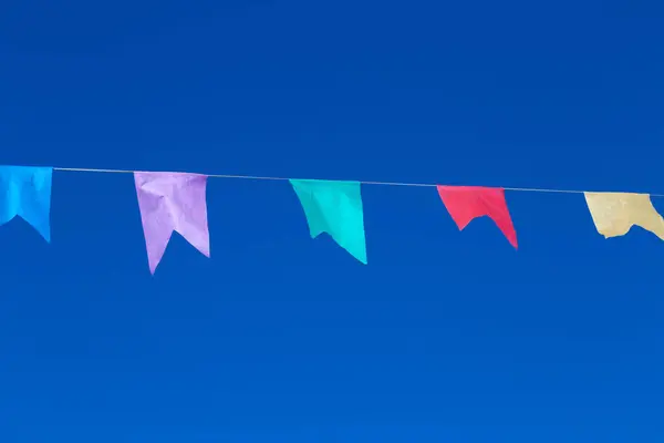 stock image A string with several colorful flags hanging with blue sky in the background. With space to write.