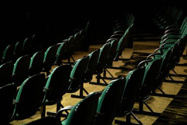 Oditoryumda birkaç sıra yeşil sandalye arkadan çekilmiş..