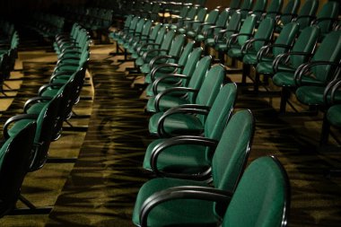 Oditoryumda birkaç sıra yeşil sandalye arkadan çekilmiş..