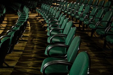 Oditoryumda birkaç sıra yeşil sandalye arkadan çekilmiş..