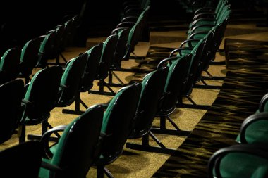 Oditoryumda birkaç sıra yeşil sandalye arkadan çekilmiş..