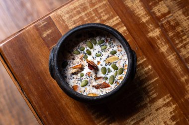  Tahta bir yüzey üzerinde fıstık sütü, fındık ve çeşitli tohumlarla dolu seramik bir kâse..