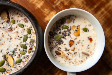 İki seramik kâse, tahıllı, fındıklı, fındıklı ve çeşitli tohumlu fıstık sütü ahşap bir yüzeyde..