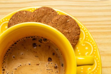 Kapuçinolu sarı fincanın yakın plan ayrıntıları ve çay tabağında biraz kurabiye..