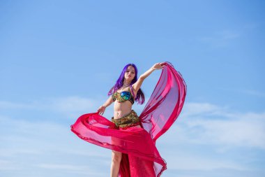 Kırmızı elbiseli, parlak etekli, akıcı kumaşlı, arka planda mavi gökyüzü olan bir dansçı..