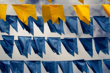 Arka planda bulutlu bir gökyüzü olan mavi ve sarı flamalarla dolu çamaşır ipleri. Kare dansı için dekorasyon.