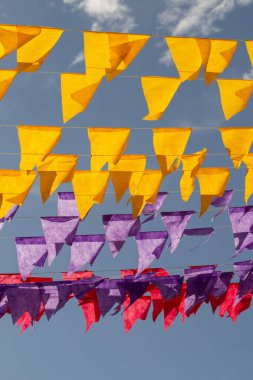 Arka planda mavi gökyüzü olan sarı, mor ve kırmızı bayraklar. Brezilya Haziran festivali arka planı.