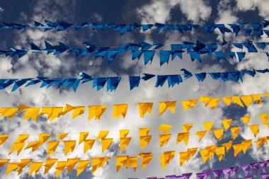 Arka planda bulutlar ve gökyüzü olan birçok renkli bayraklı çamaşır ipleri. Kare dansı için dekorasyon - tipik bir Brezilyalı partisi.