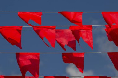 İplerde asılı kırmızı bayraklar, arka planda mavi gökyüzü.