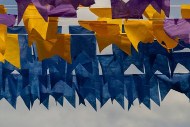 Üzerlerinde renkli flamalar asılı bazı ipler. Tam kare. Arka planda mavi gökyüzü.