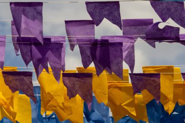 Üzerlerinde renkli flamalar asılı bazı ipler. Tam kare. Arka planda mavi gökyüzü.