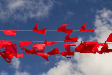 İplerde asılı kırmızı bayraklar, arka planda mavi gökyüzü.