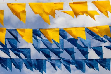 Arka planda bulutlu bir gökyüzü olan mavi ve sarı flamalarla dolu çamaşır ipleri.