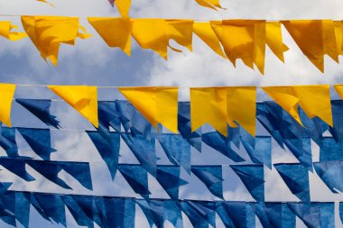 Arka planda bulutlu bir gökyüzü olan mavi ve sarı flamalarla dolu çamaşır ipleri.