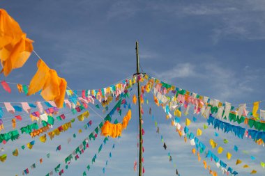 Renkli flamalar sallanan, rüzgarda sallanan, arka planda mavi bir gökyüzü olan bir dizi ip. Kare dansı ve Festa Junina için dekorasyon -