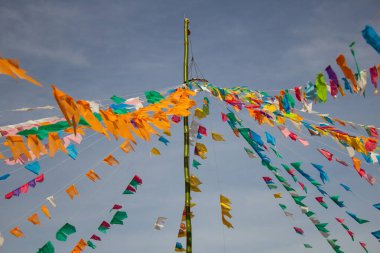 Renkli flamalar sallanan, rüzgarda sallanan, arka planda mavi bir gökyüzü olan bir dizi ip. Kare dansı ve Festa Junina için dekorasyon -