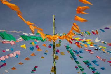 Renkli flamalar sallanan, rüzgarda sallanan, arka planda mavi bir gökyüzü olan bir dizi ip. Kare dansı ve Festa Junina için dekorasyon -