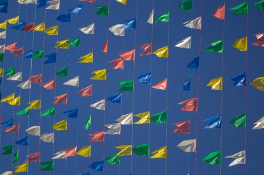 Renkli flamalarla asılı çamaşır iplerinin fotoğrafı, rüzgarda sallanan arka planda mavi gökyüzü. Haziran festivali için dekorasyon.