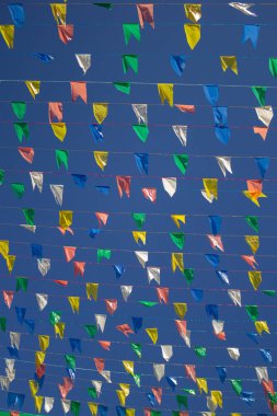 Üzerinde renkli flamalar asılı birkaç çamaşır ipinin panoramik fotoğrafı, rüzgarda sallanan arka planda mavi gökyüzü.