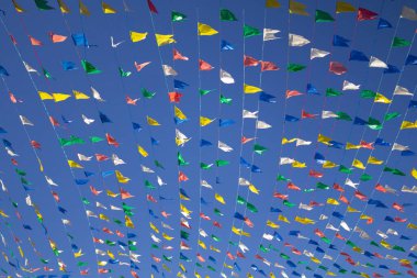  Renkli flamalarla asılı çamaşır iplerinin fotoğrafı, rüzgarda sallanan arka planda mavi gökyüzü. Haziran festivali için dekorasyon.