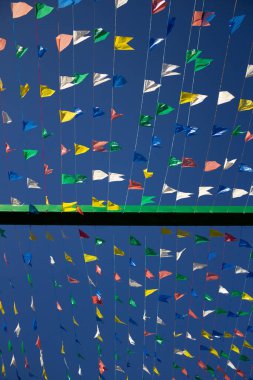 Üzerinde renkli flamalar asılı birkaç çamaşır ipinin fotoğrafı. Rüzgarda sallanan ve arka planda mavi gökyüzü olan. Haziran festivali için dekorasyon.