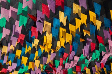 Dışarıda sallanan renkli bayraklar rüzgarda dans ediyor arka planda bulanık bir binanın camları var..