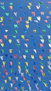 Açık mavi gökyüzüne karşı rüzgarda hareket eden ipe bağlanmış birkaç renkli bayrak