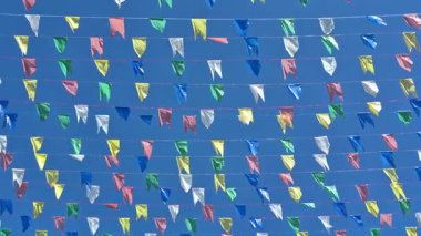 Açık mavi gökyüzüne karşı rüzgarda hareket eden ipe bağlanmış birkaç renkli bayrak.